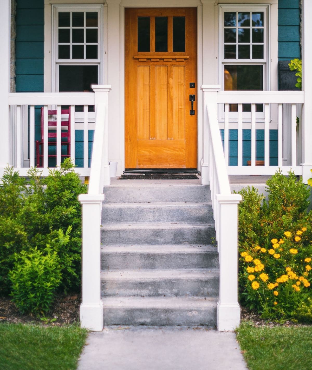 Wooden craftsman front door on a porch with white railings and concrete steps