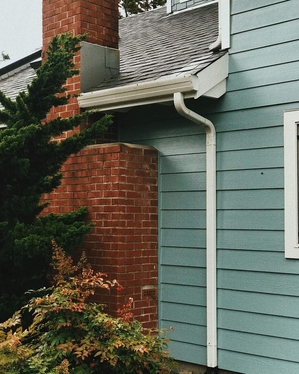 White rain gutter and downspout on a house with blue lap siding and a brick chimney