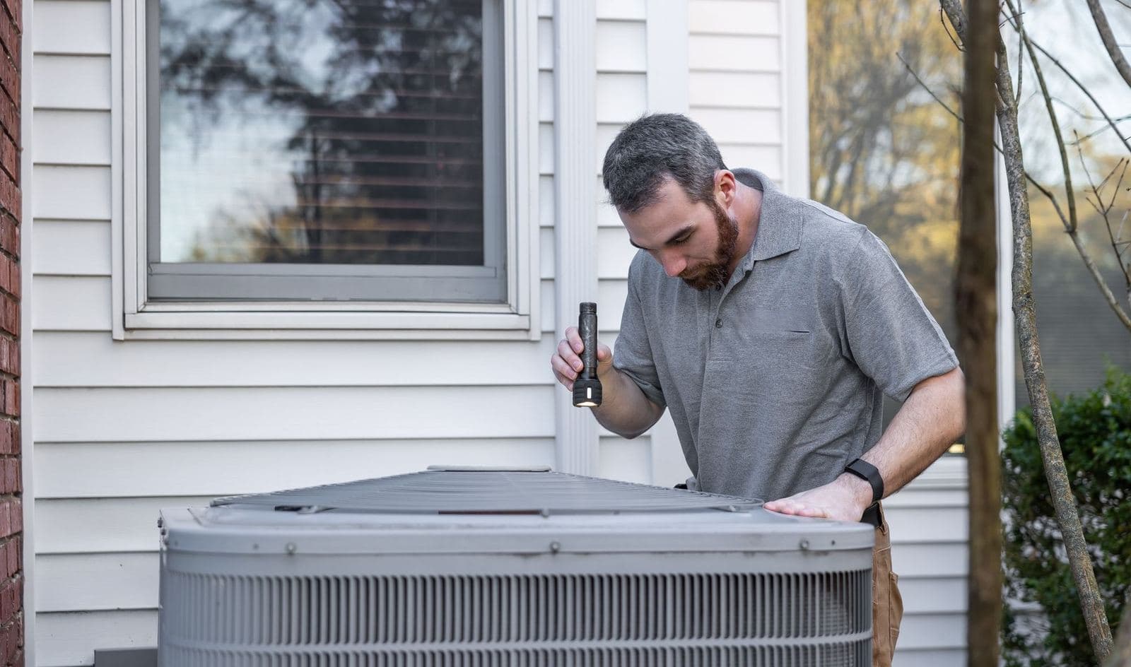 Technician inspecting an outdoor central air conditioner beside a house