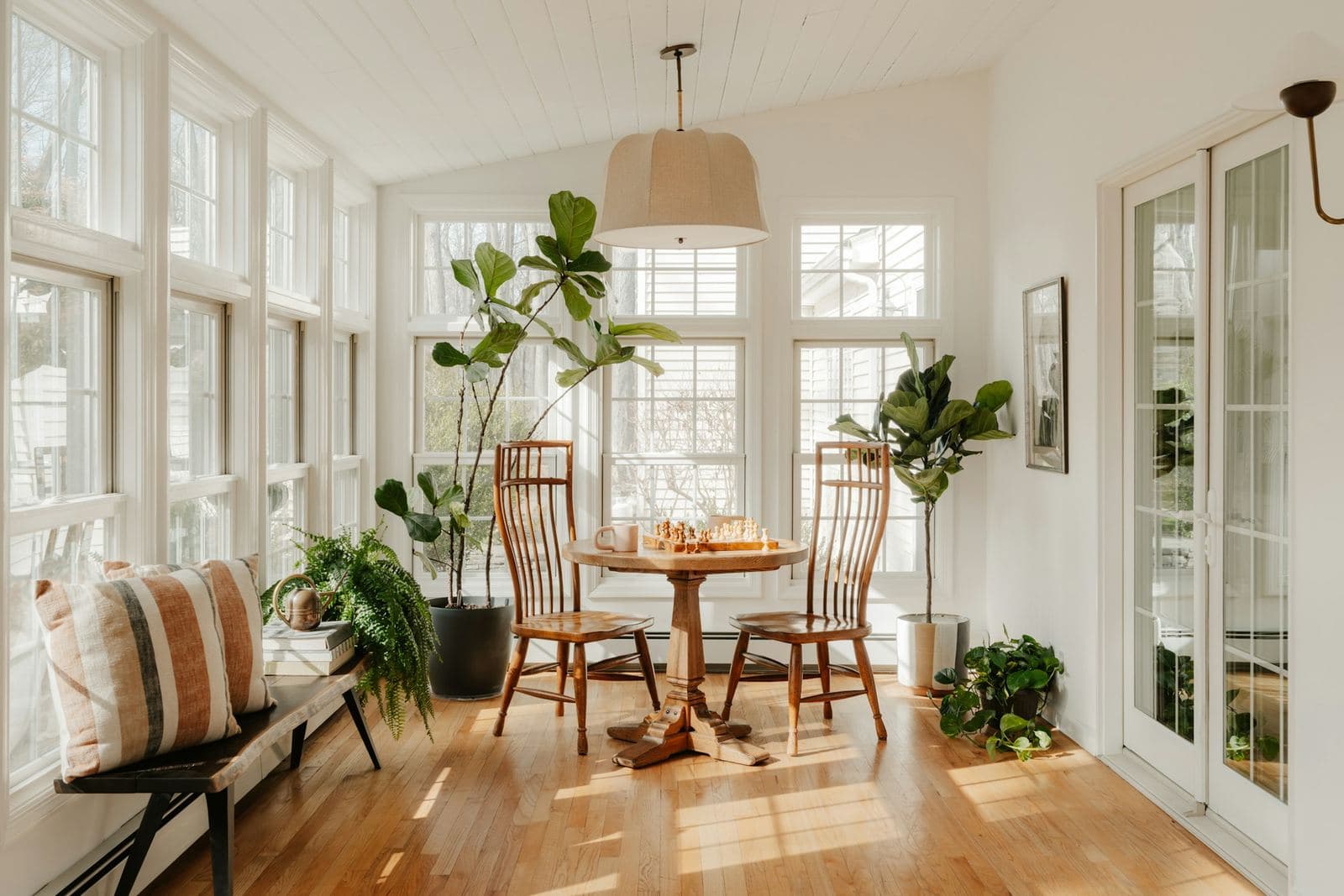 Bright sunroom with walls of windows, hardwood floor, plants and a small table