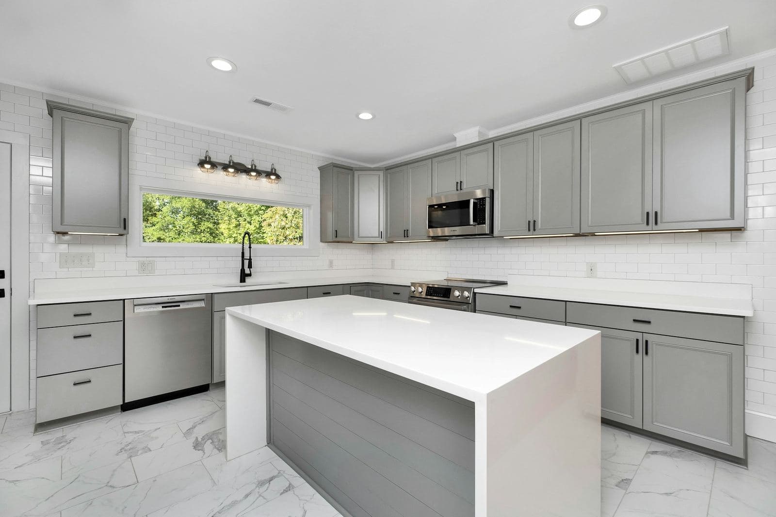 Kitchen with gray shaker cabinets, black hardware and a white island