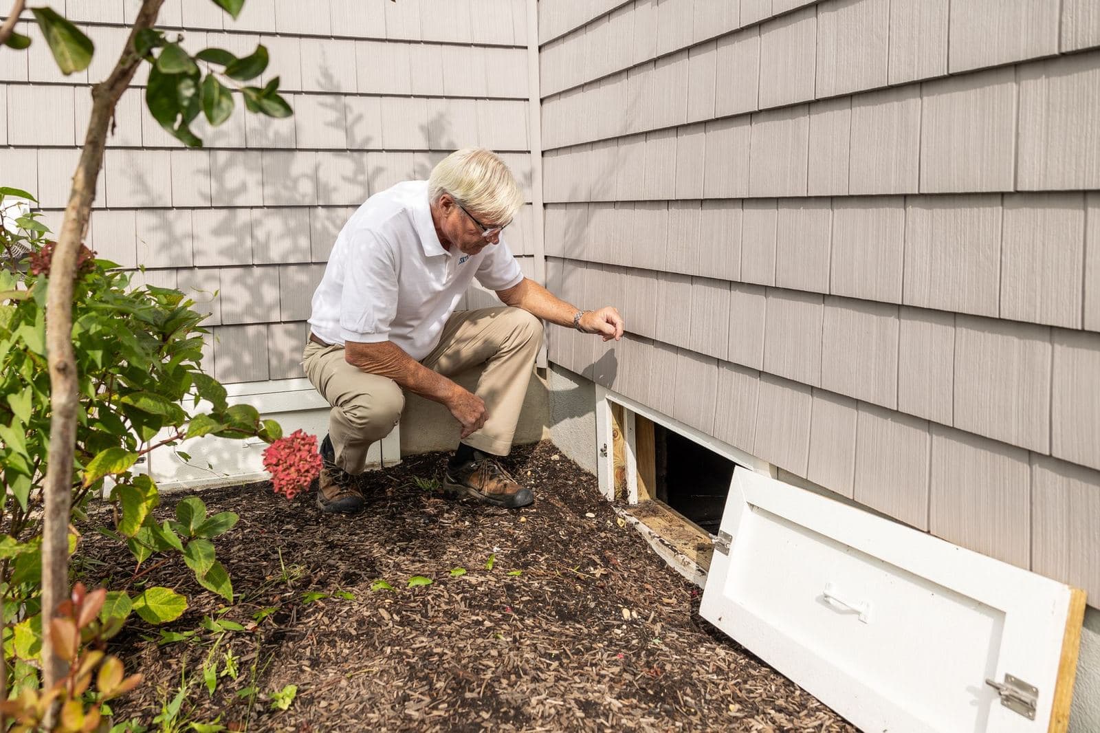 Inspector checking a home's crawl space access beside the foundation