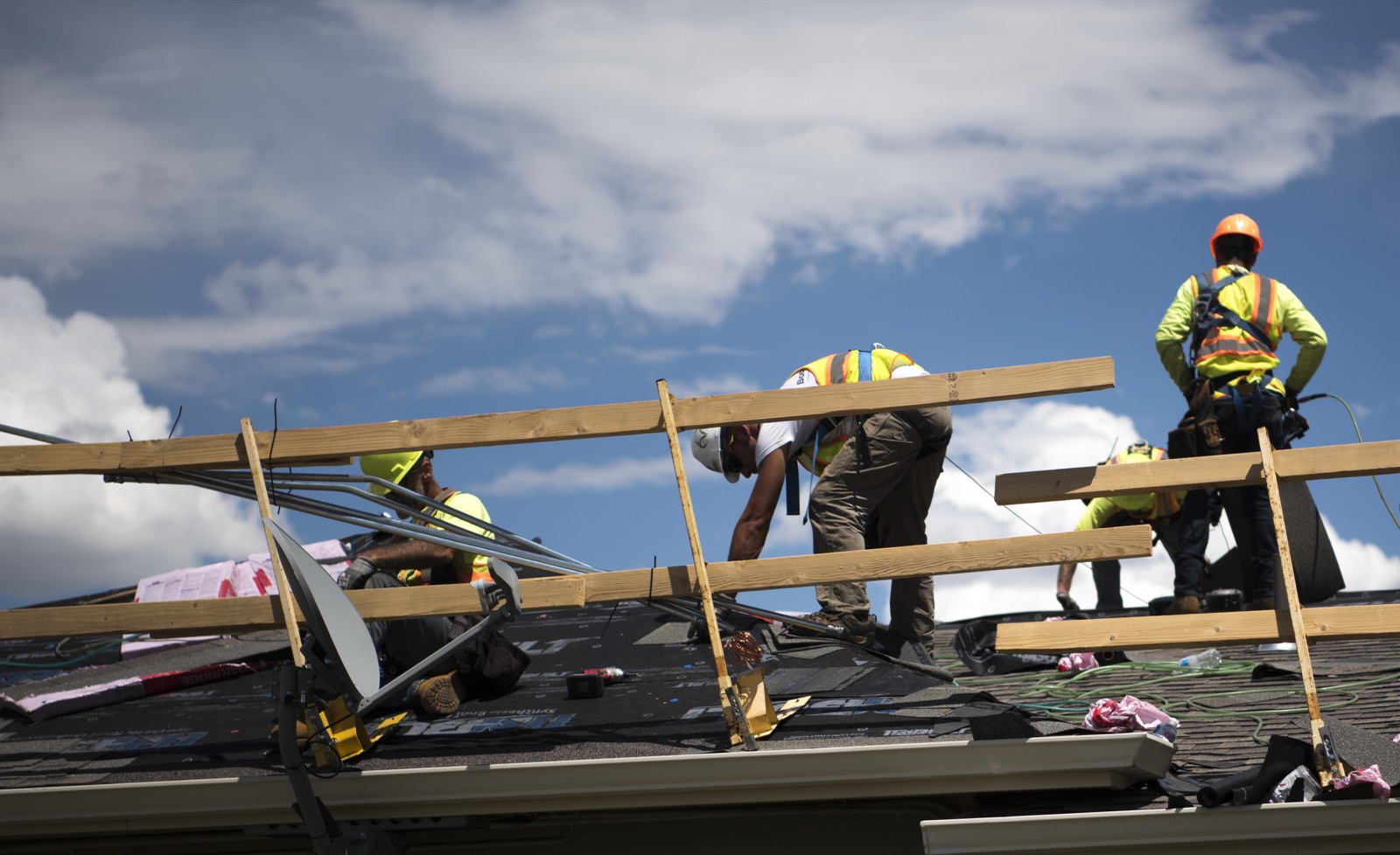 Roofing crew in safety harnesses replacing hail-damaged asphalt shingles on a home in Colorado